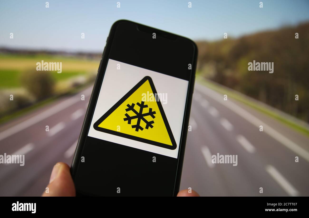 Visualizza il telefono cellulare con il simbolo di pericolo per basse temperature giallo triangolare internazionale. Sfondo dell'autostrada sfocato. Foto Stock