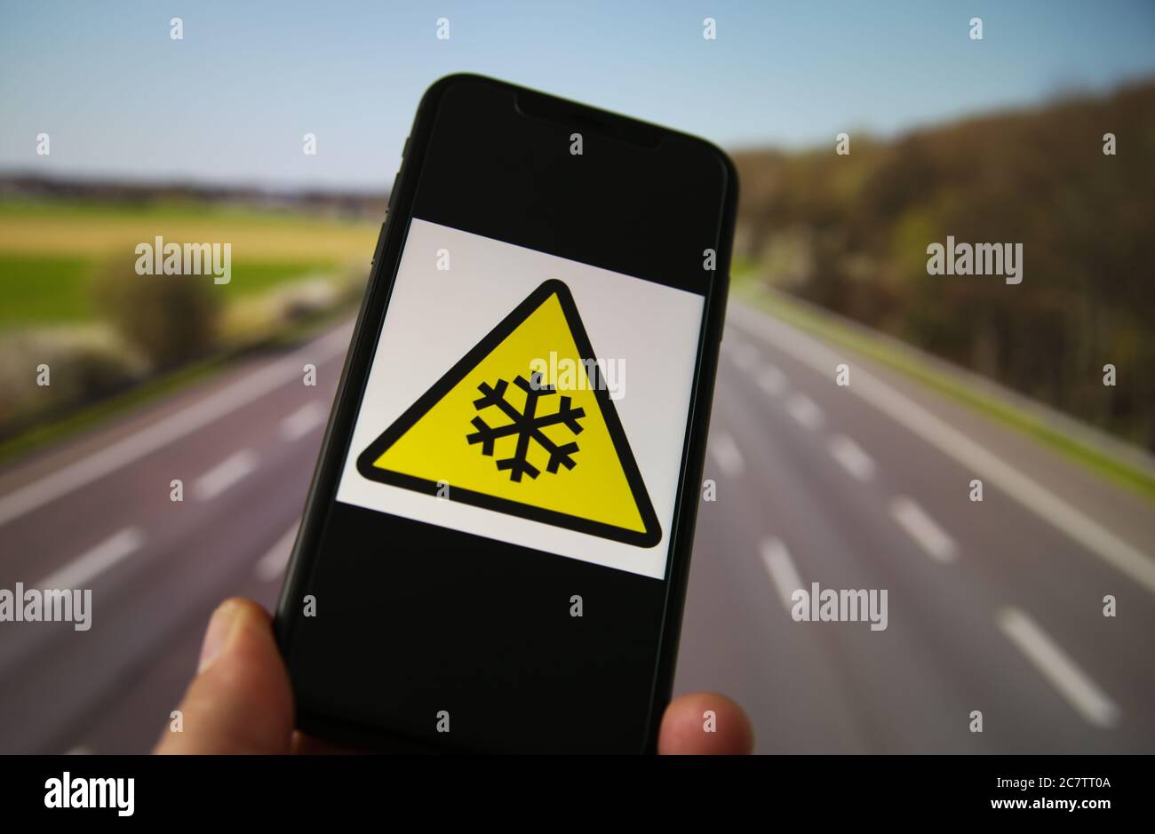 Visualizza il telefono cellulare con il simbolo di pericolo per basse temperature giallo triangolare internazionale. Sfondo dell'autostrada sfocato. Foto Stock