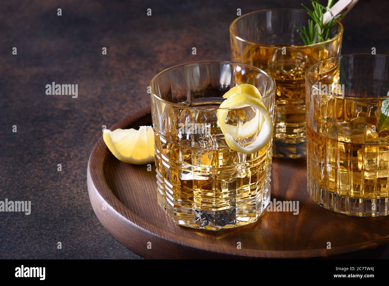 Tre bicchieri di whisky freddo serviti su rocce con rosmarino, bucce di limone su sfondo marrone. Spazio di copia. Foto Stock