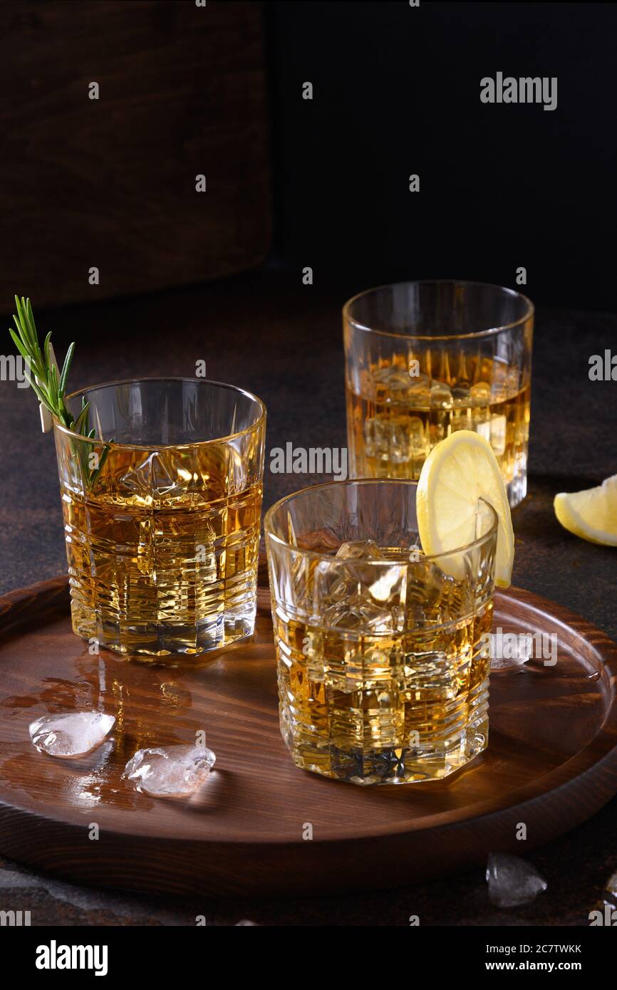 Tre bicchieri di whisky freddo con rosmarino, bucce di limone su sfondo marrone scuro. Orientamento verticale. Foto Stock