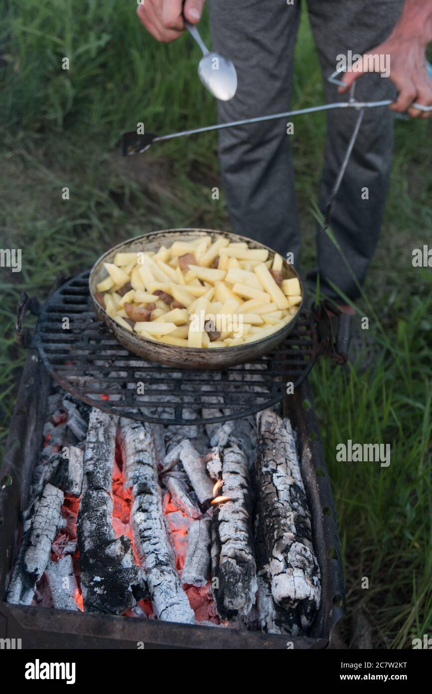 Patate crude tagliate a fette in una padella sopra carbone. Barbecue all'aperto. Preparazione di cibo Foto Stock