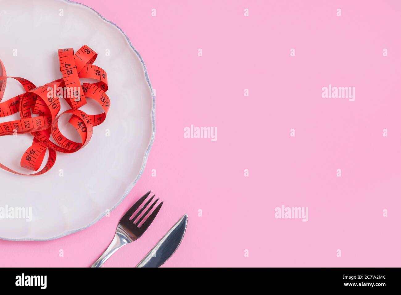 Concetto di dieta. Vista sopra le posate argentate con nastro di misurazione su piastra bianca su sfondo rosa pastello Foto Stock