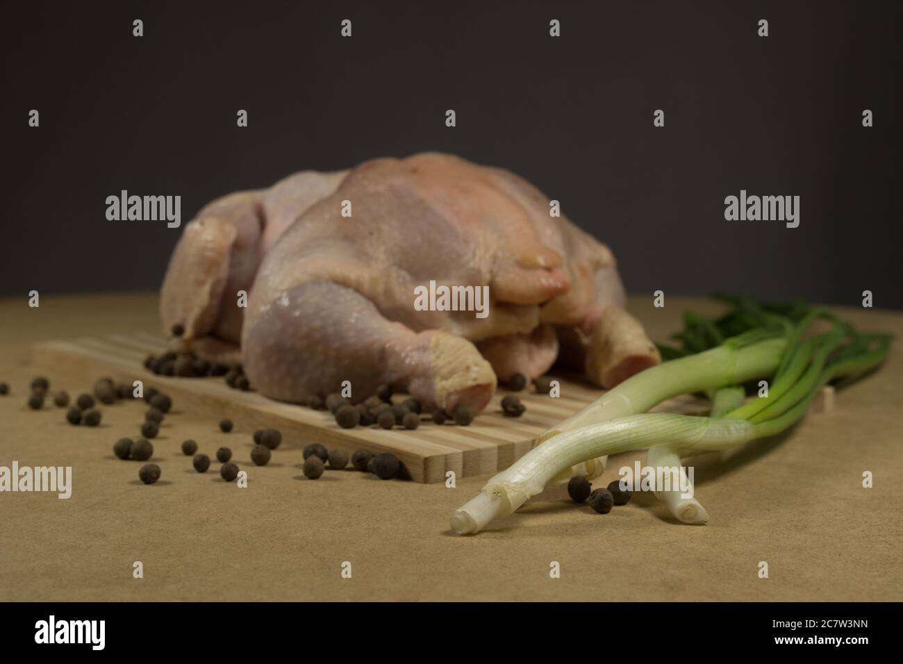 Carcassa di pollo cruda con spezie ed erbe su un tagliere su un tavolo di legno Foto Stock
