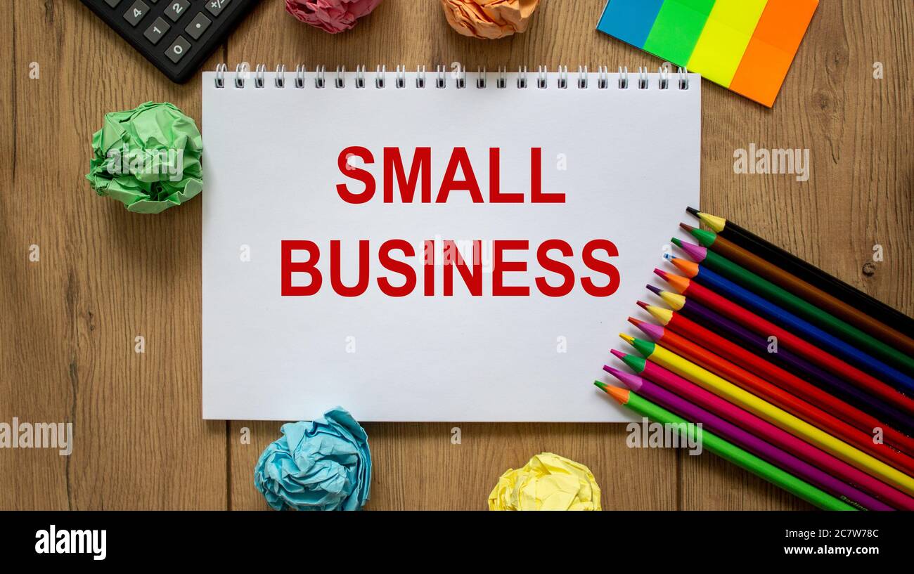 Nota bianca con iscrizione 'piccola impresa' su bel tavolo di legno, carta colorata, matite colorate, e calcolatrice. Concetto aziendale. Foto Stock