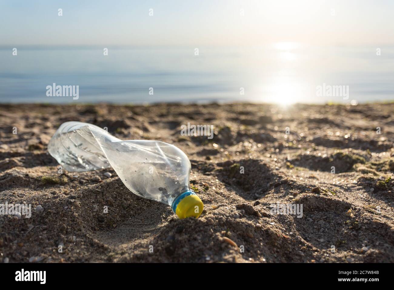 Bottiglia di plastica sdraiata sulla spiaggia vicino all'acqua, inquinamento marino sfondo Foto Stock