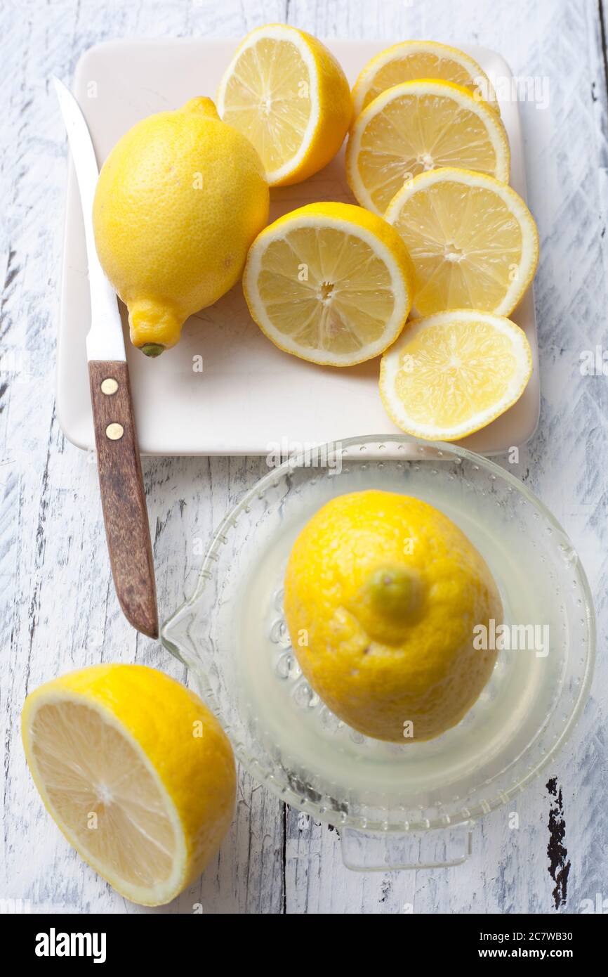Primo piano di limoni e fette in un piatto con un coltello su un tavolo da tavola bianca con un estrattore di succo Foto Stock