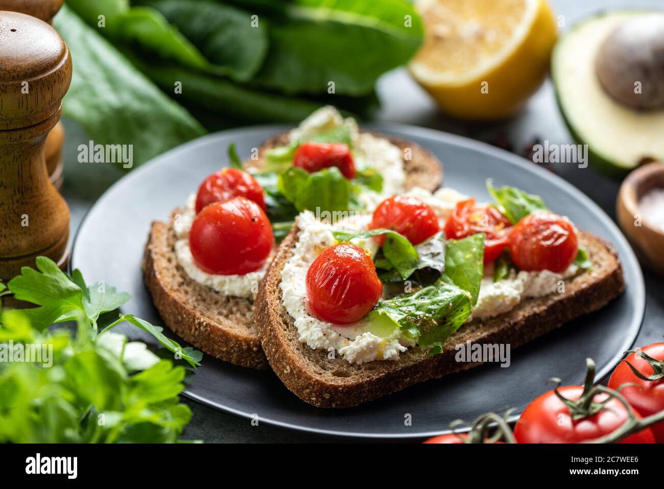 Gustoso sandwich con ricotta bianca, pomodori arrostiti e basilico guarnito con pepe e olio d'oliva schiacciati Foto Stock