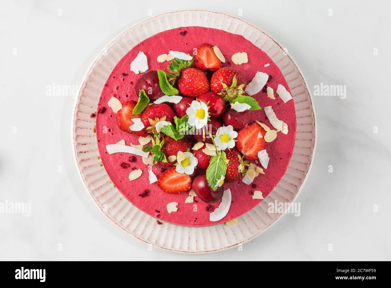 cheesecake crudo di frutti di bosco di fagiolo, di anacardi, ciliegie, fragole, cocco, mandorle e datteri con frutti di bosco e fiori freschi. delizioso dessert. top vie Foto Stock