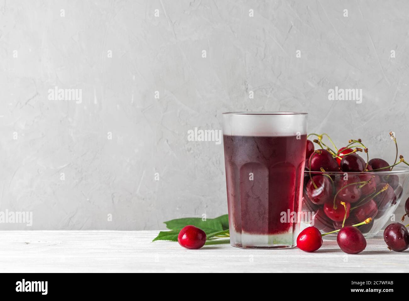 Succo di ciliegia in un bicchiere con frutti di bosco freschi su sfondo bianco. Rinfresco estivo drink. Bevanda sana Foto Stock