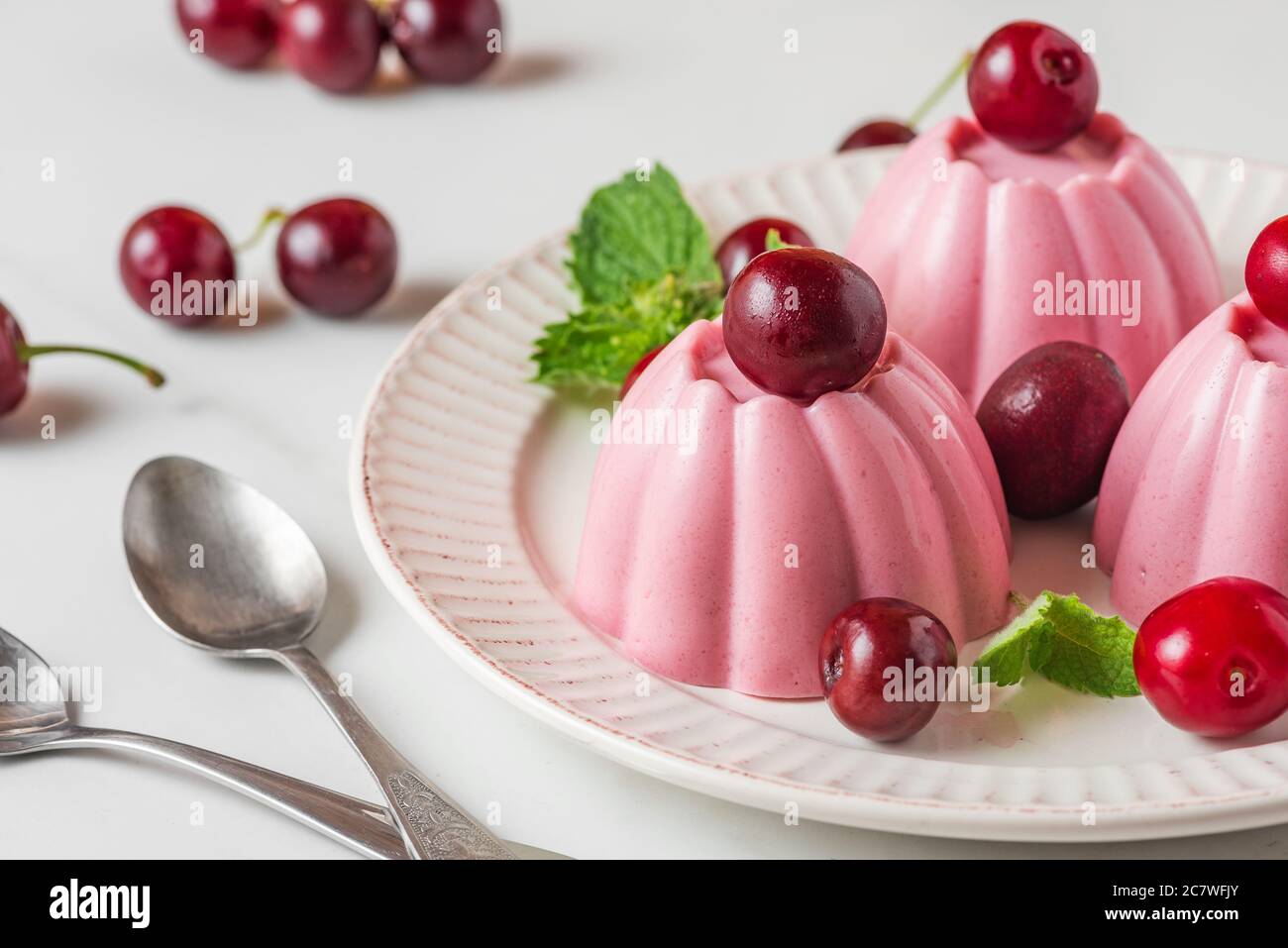 Dessert di panna cotta di ciliegia con frutti di bosco freschi, menta e cucchiai. Dessert salutari all'italiana. Primo piano Foto Stock