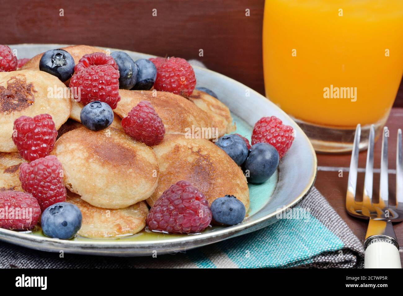 Mini frittelle con frutti di bosco e succo d'arancia su tavolo di legno Foto Stock