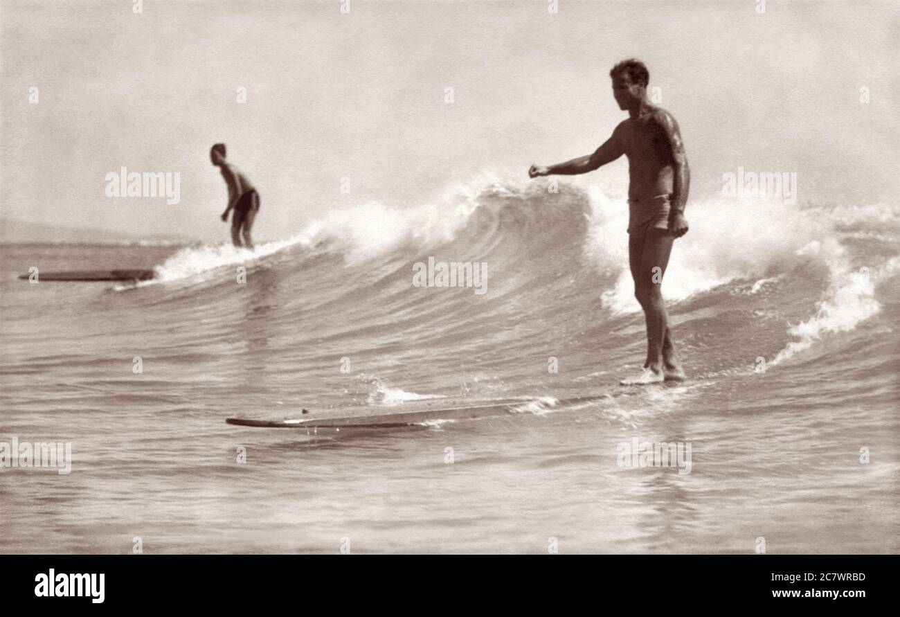 Due surfisti che cavalcano tavole da surf in legno a Waikiki a Honolulu, territorio delle Hawaii negli anni '30. Foto Stock