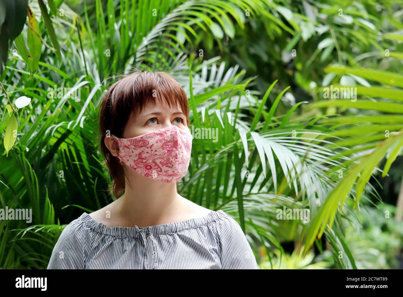 Donna in maschera medica protettiva in una giungla. Concetto di quarantena durante la pandemia di coronavirus covid-19 in un clima tropicale Foto Stock