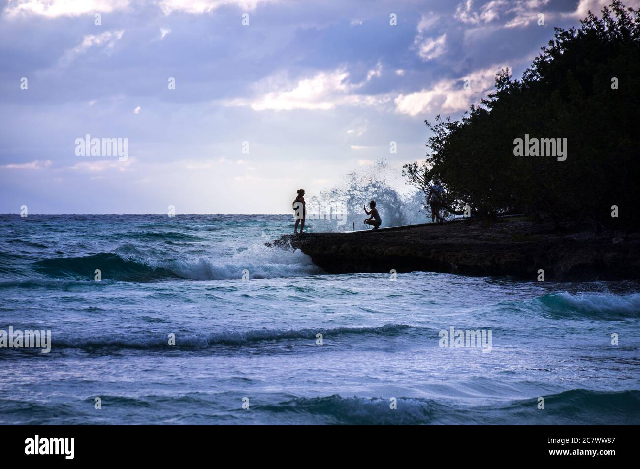 Un gruppo di turisti che osservano il tramonto sulle onde ripide di roccia tra le onde curling turchesi. Foto Stock