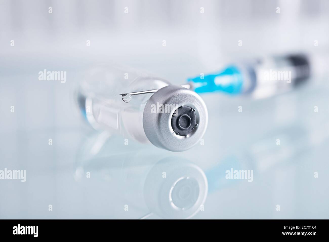Shot di chiusura di una siringa e di un flaconcino di vetro chiuso con liquido trasparente su una superficie bianca Foto Stock