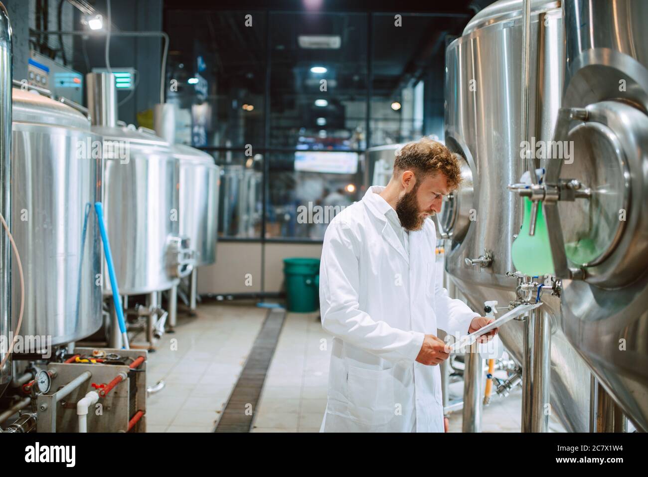 Esperto di tecnologia maschile caucasica in tuta bianca che opera in macchina di produzione in fabbrica alimentare e che fa controllo di qualità e tiene checklist Foto Stock