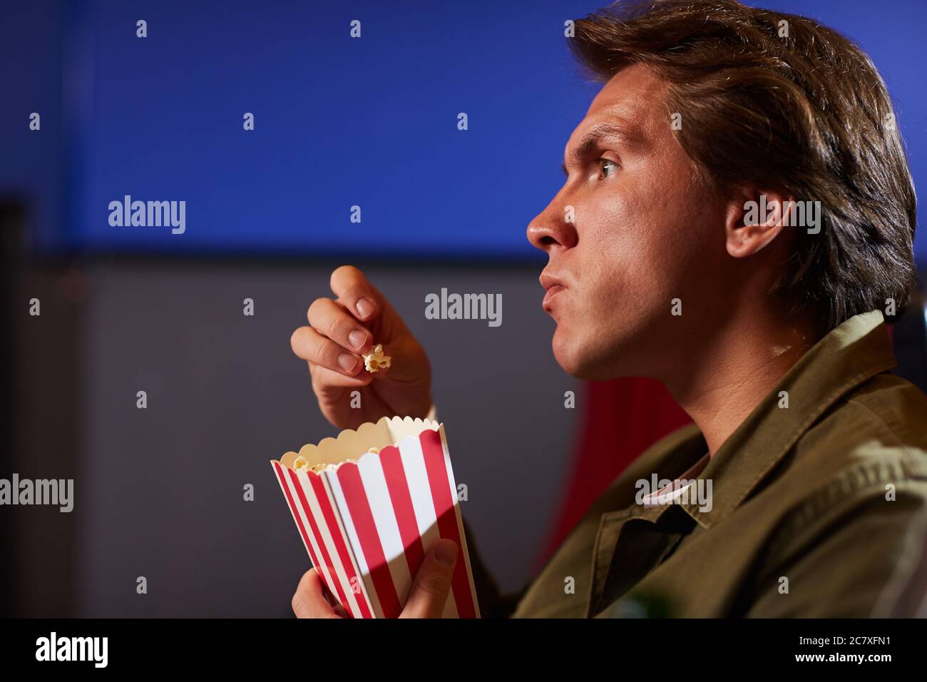 Vista laterale ritratto di giovane uomo che mangia popcorn mentre guardi il film in cinema solo teatro, copia spazio Foto Stock