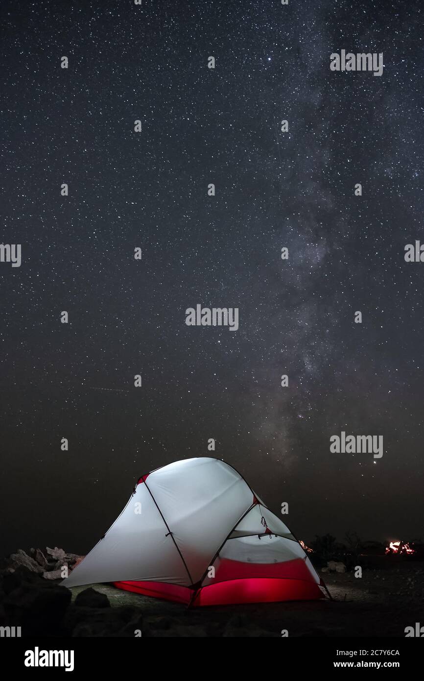 Una tenda si illumina sotto un cielo notturno pieno di stelle. Foto Stock