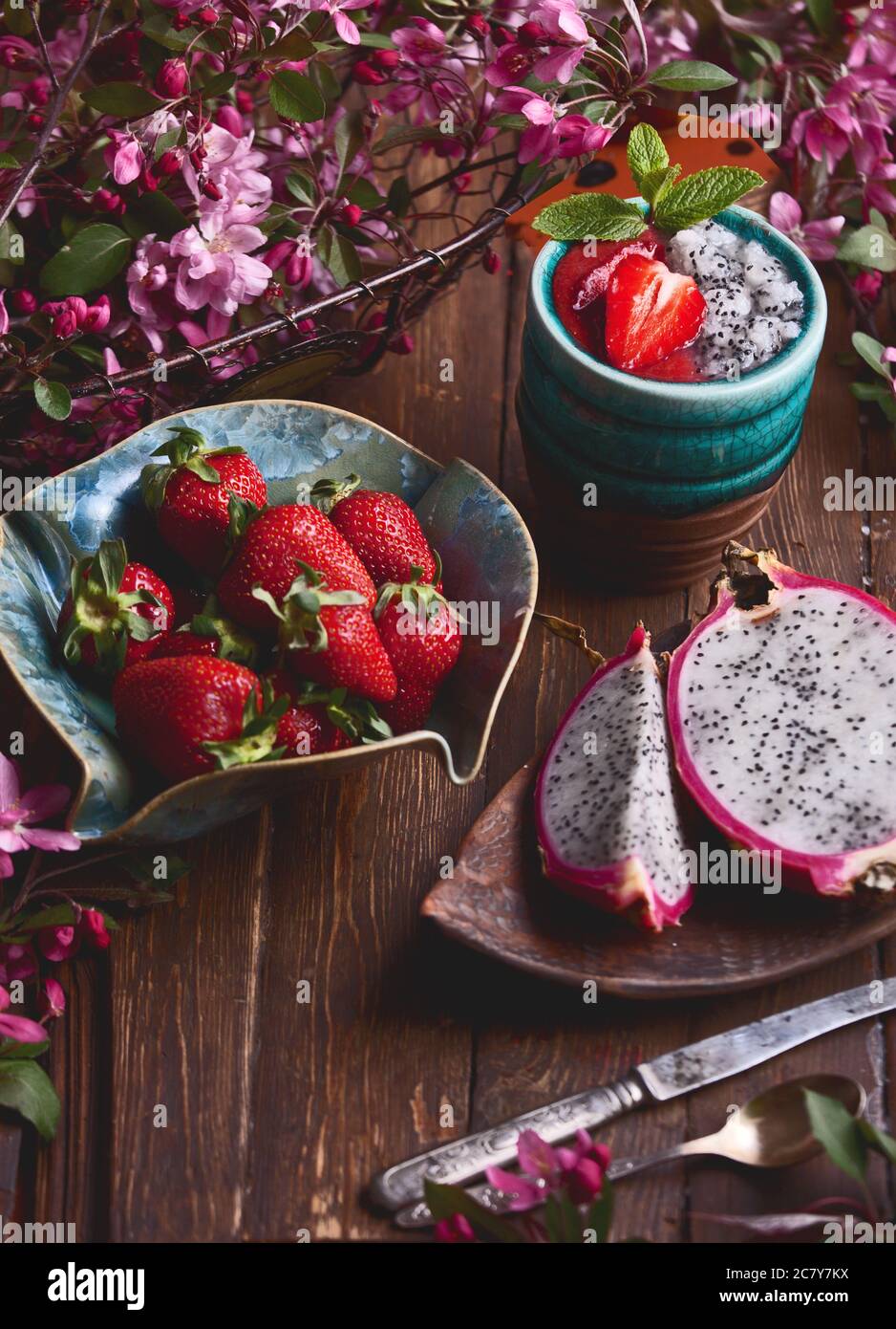 flatlay food sfondo - vuoto bordo di legno scuro con frutta di drago, fragole, frullato fresco e fiori rosa, copia spazio per il testo Foto Stock
