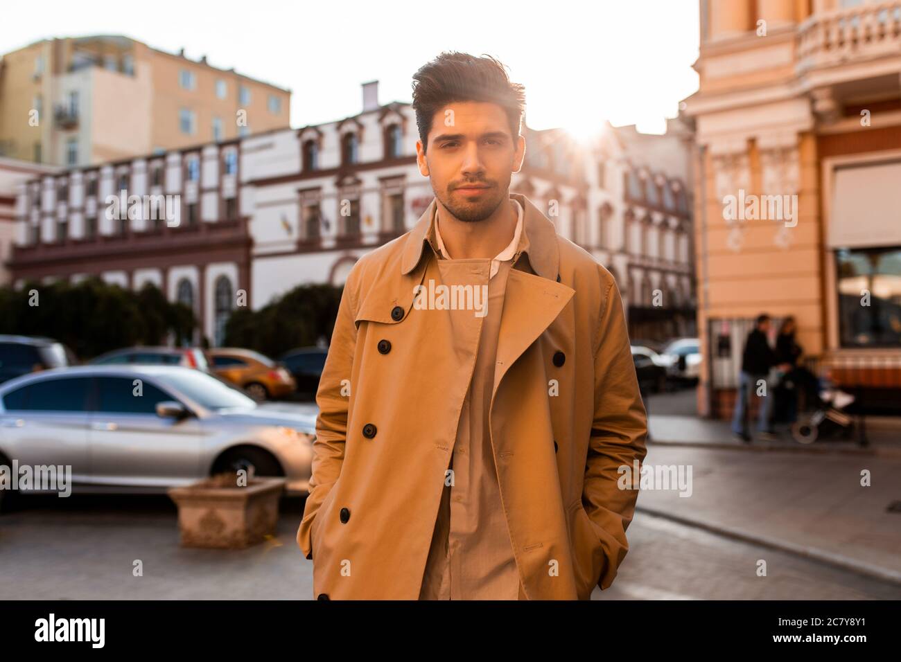 Giovane uomo casual bello in trench cappotto guardando con sicurezza in macchina fotografica su strada Foto Stock