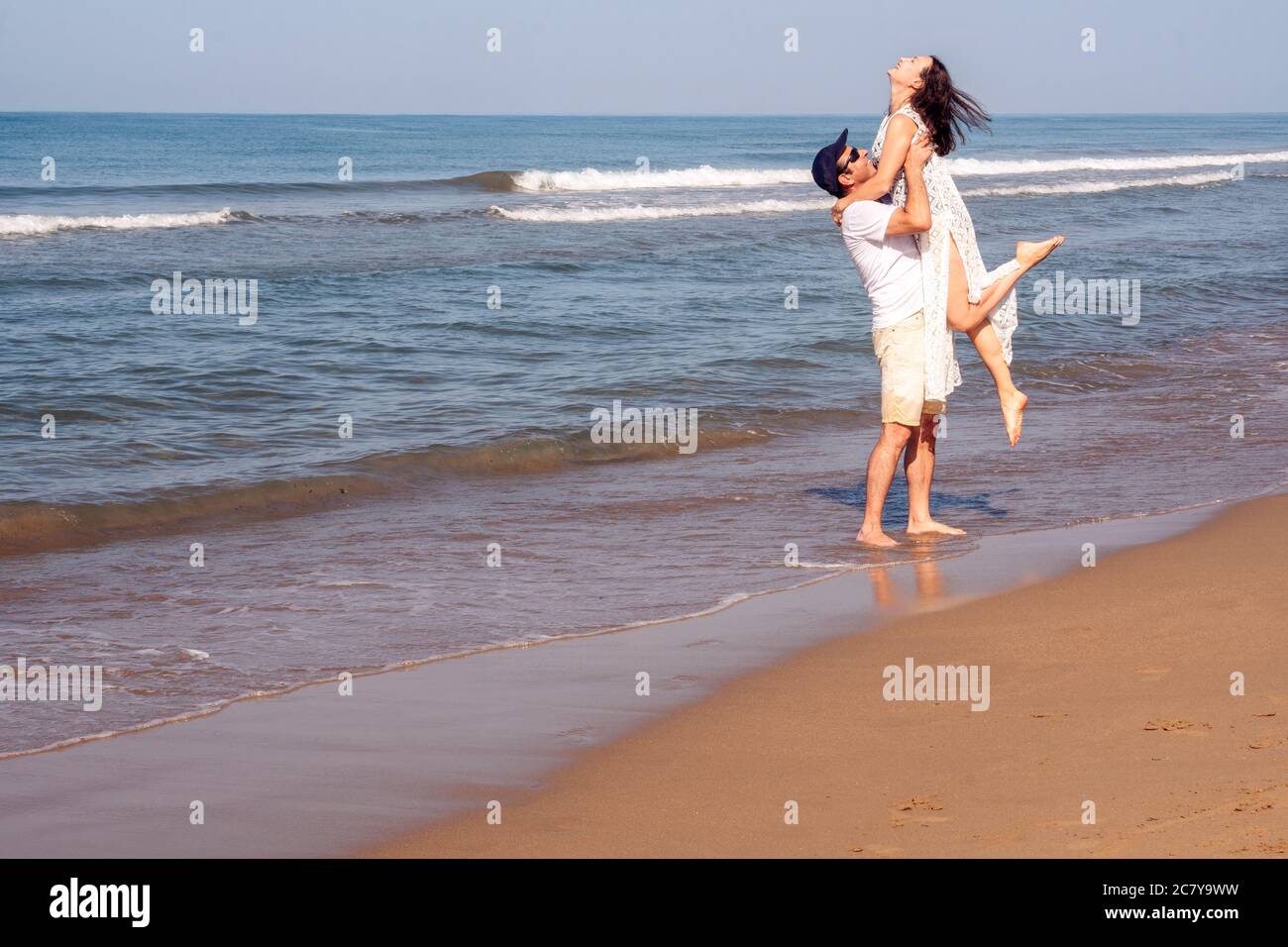 Felice coppia alla spiaggia di sabbia dorata. Uomo che tiene la donna tra le braccia con amore Foto Stock