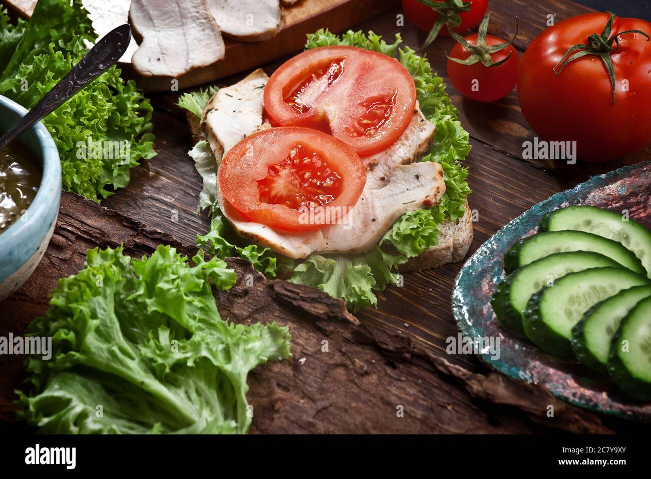 sandwich di carne di tacchino con pomodori freschi, insalata di lattuga verde e cetrioli su sfondo rustico di legno scuro, nessuno Foto Stock