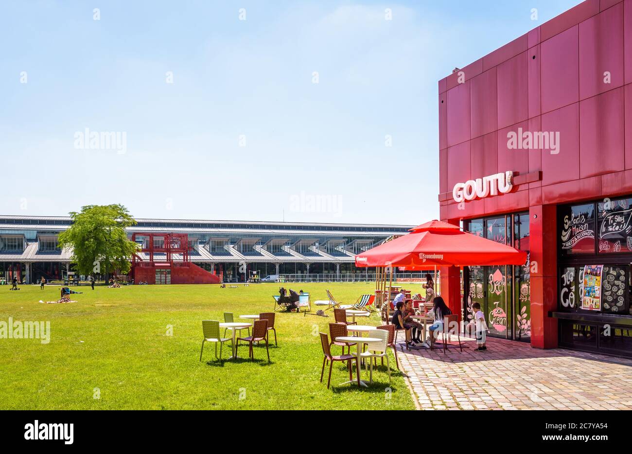 La gente può godersi una giornata di sole nel Parc de la Villette di Parigi, prendere il sole sul prato lungo la Grande Halle o fare uno spuntino sulla terrazza di uno snack bar. Foto Stock