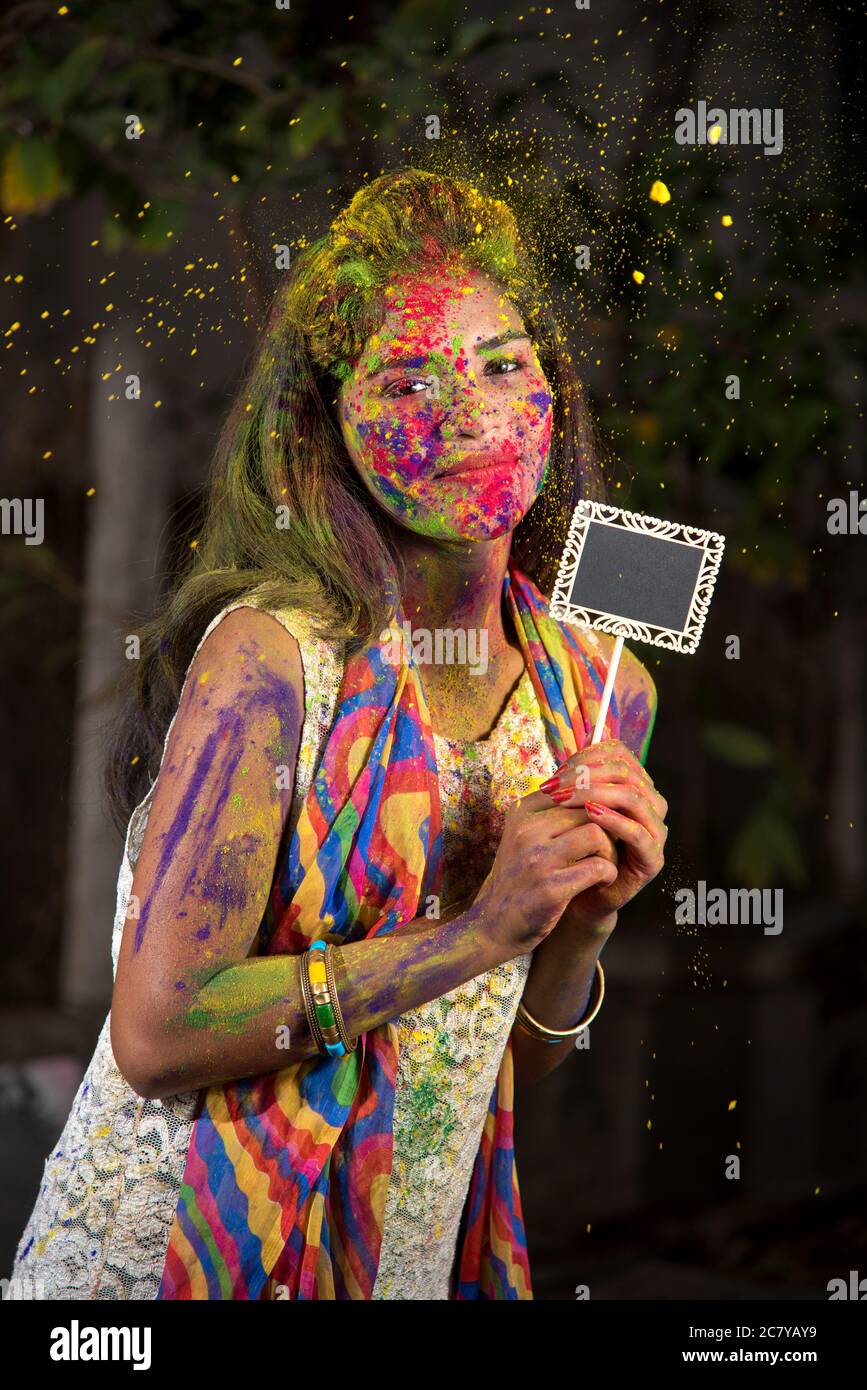 Giovane ragazza che tiene la piccola tavola in occasione del festival Holi con volti dipinti con colori in polvere, con un colore splash. Foto Stock