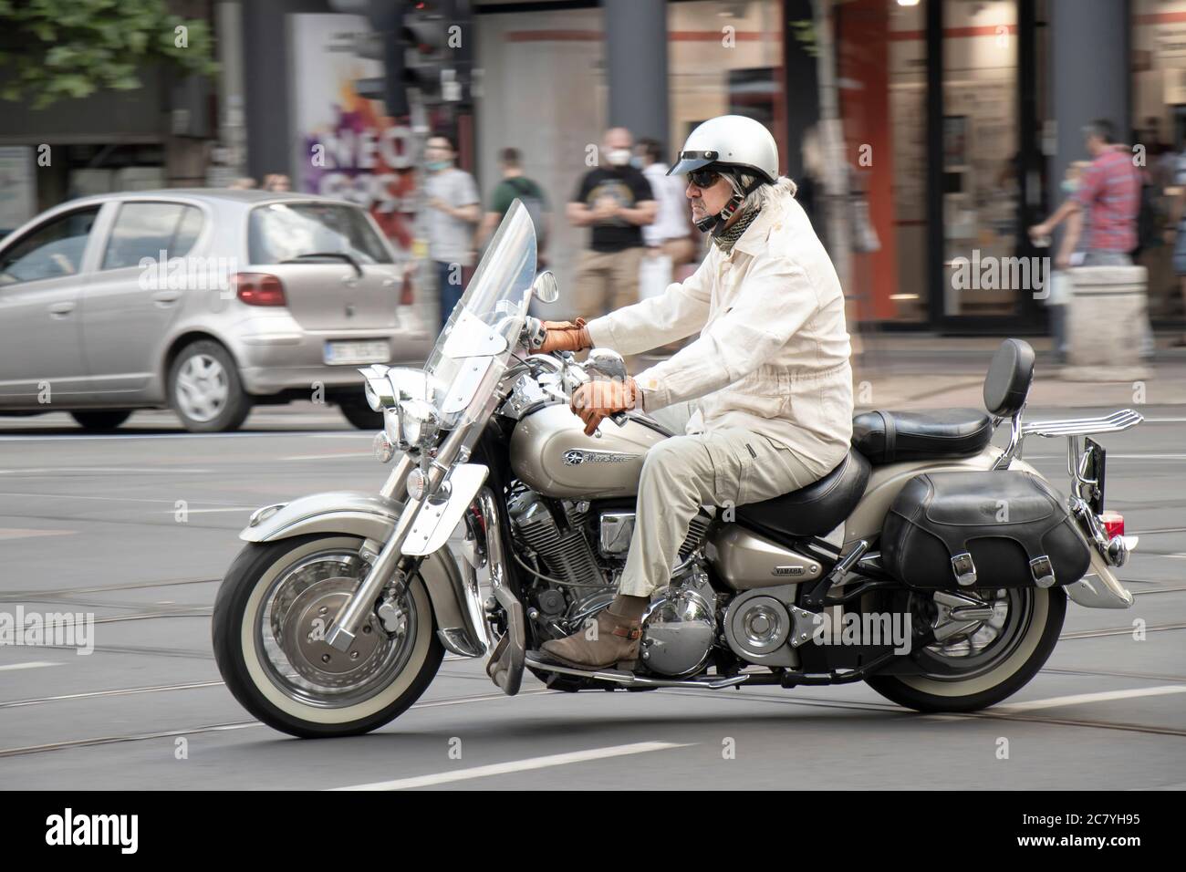 Belgrado, Serbia - 16 luglio 2020: Uomo maturo in outfit beige chiaro che cavalcano una motocicletta a due posti con borse laterali a sella sul traffico cittadino, lato v Foto Stock