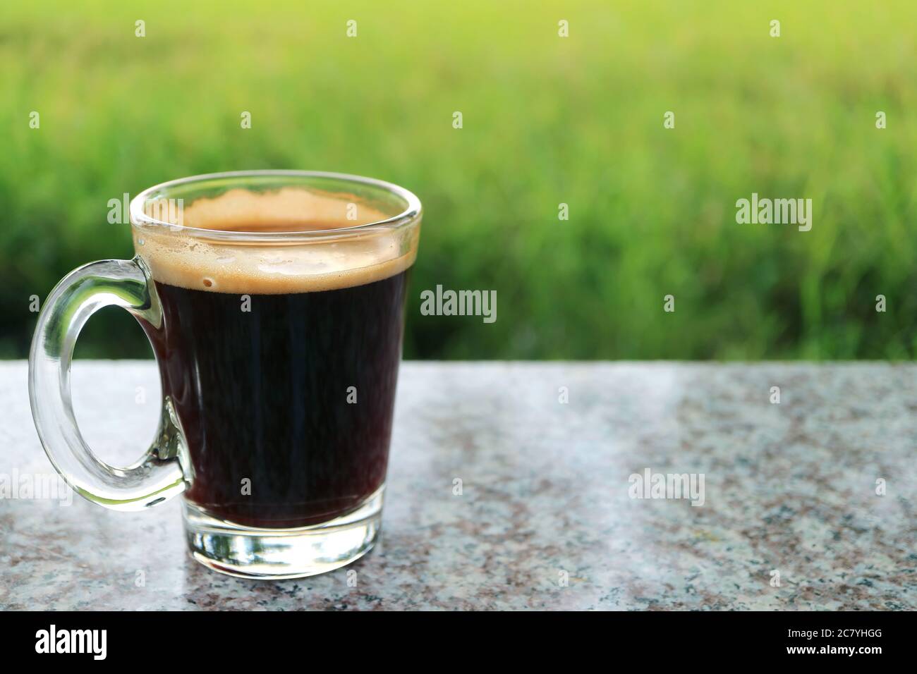Un caffè nero caldo in un vetro trasparente con prato verde sfocato in background Foto Stock