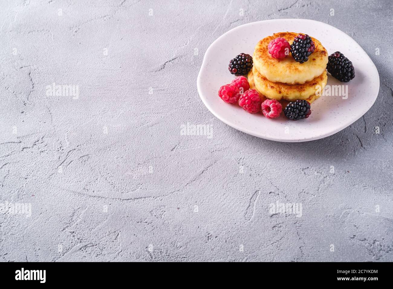 Frittelle al formaggio di cottage, frittelle di cagliata dessert con lampone e frutti di mora in piastra su fondo di pietra in cemento, angolo di vista spazio copia Foto Stock