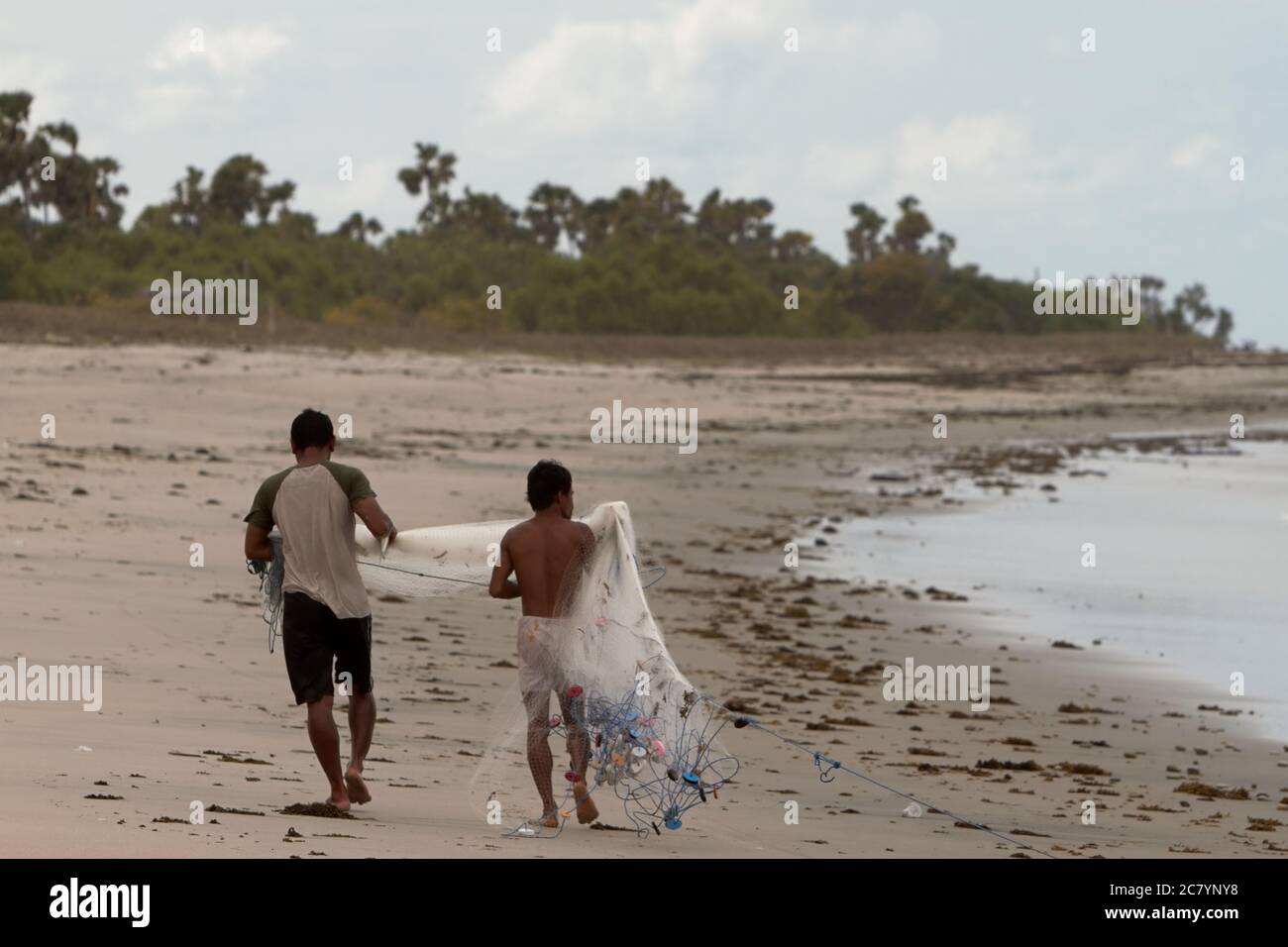 Pescatori che trasportano reti da pesca mentre camminano sulla spiaggia di Kalala a Wula, Wula Waijelu, Sumba orientale, Nusa Tenggara orientale, Indonesia. Foto Stock