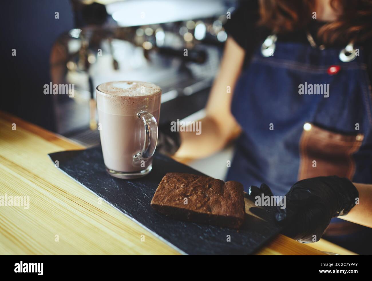 Barista che indossa guanti medici in lattice nero, rendendo rosa matcha latte con latte. Barista preparando una bevanda gustosa e una torta brownie Foto Stock