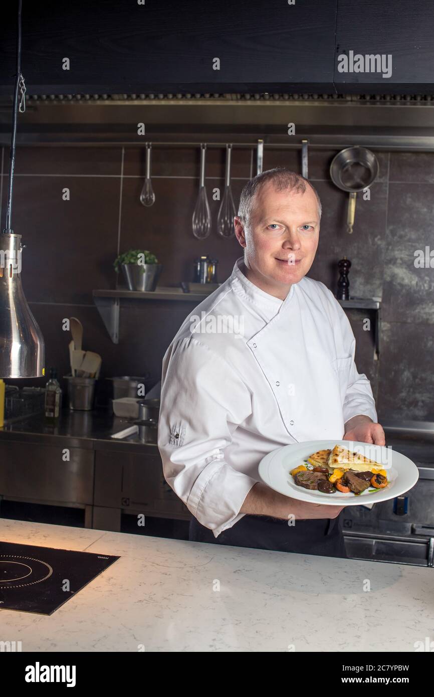 Ritratto di un maschio sorridente chef con il cibo cotto in piedi in cucina Foto Stock