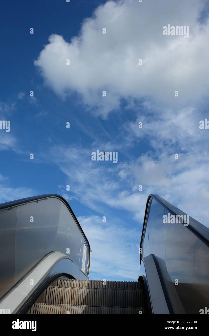 La scala mobile all'aperto si solleva verso il cielo azzurro soleggiato con nuvole bianche. Un aereo che vola nel cielo: Libertà, successo, concetto di promozione Foto Stock