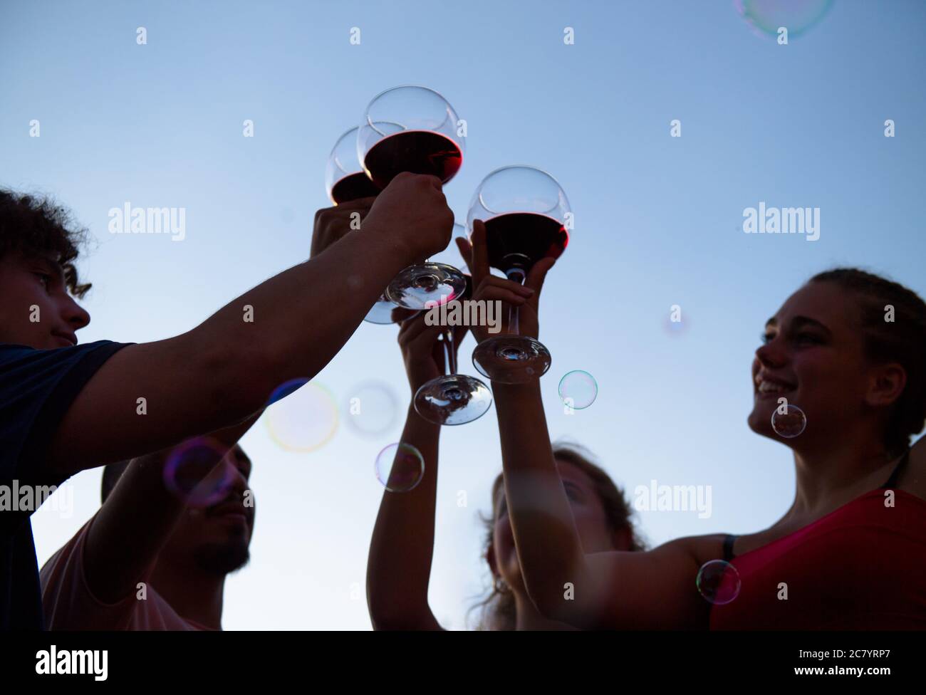 Quattro ragazzi tostano con un bicchiere di vino al tramonto sulla terrazza Foto Stock