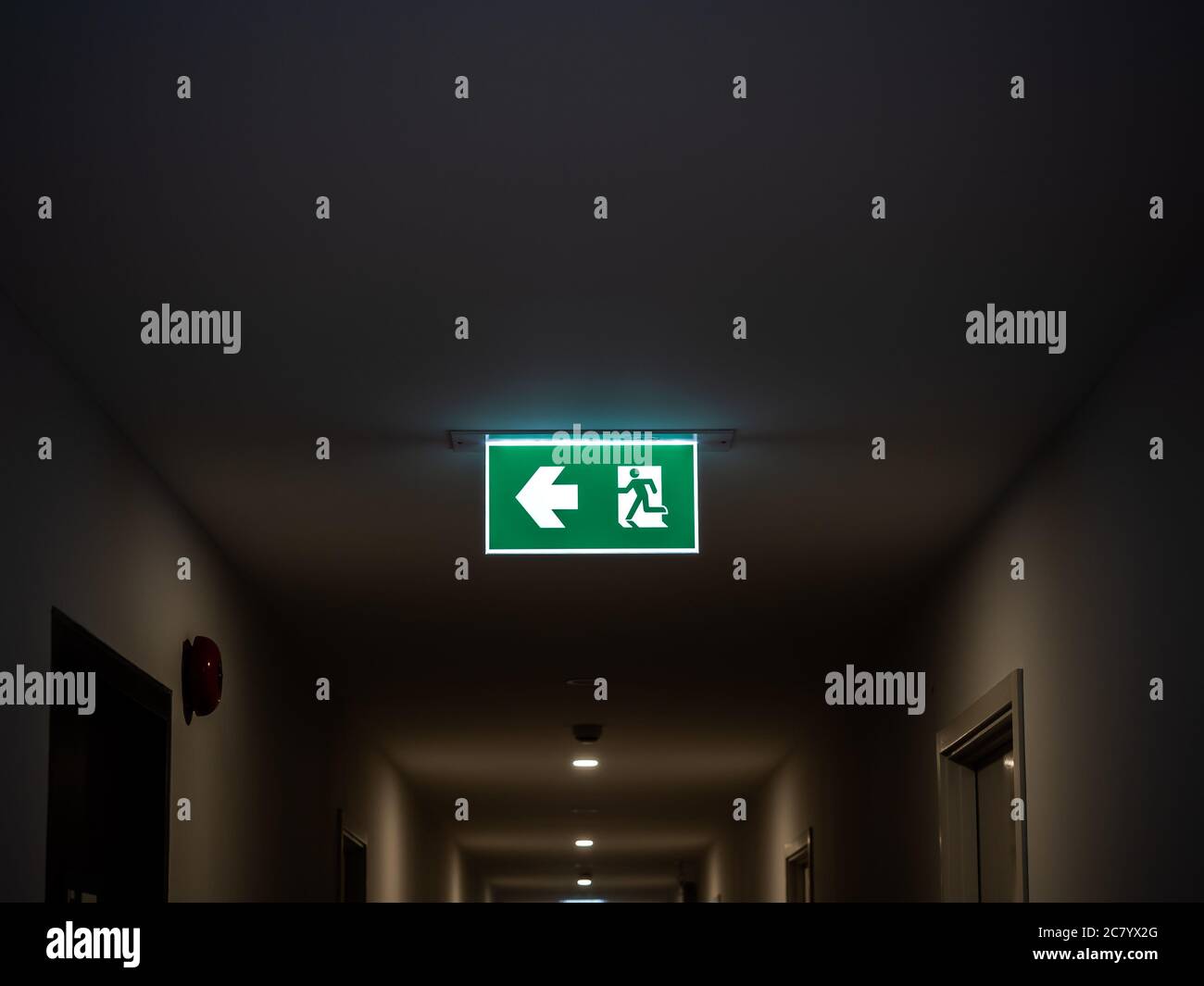 Uscita antincendio. Cartello verde illuminato di uscita appeso al soffitto in un edificio moderno al buio dell'appartamento. Foto Stock
