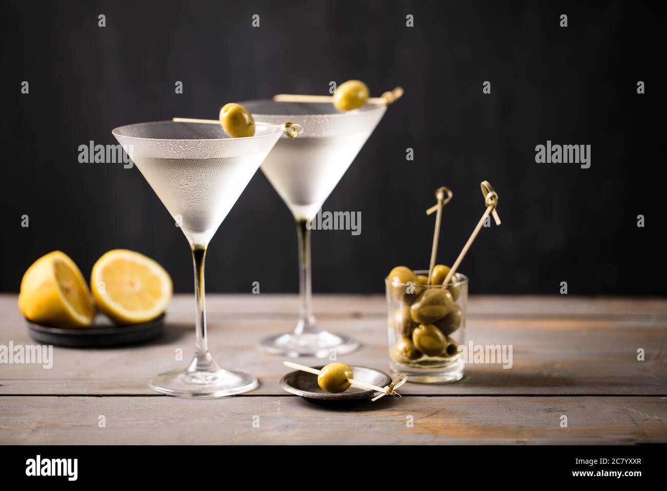 Cocktail martini ghiacciato servito con un set di olive su un bar grigio in legno con sfondo scuro Foto Stock