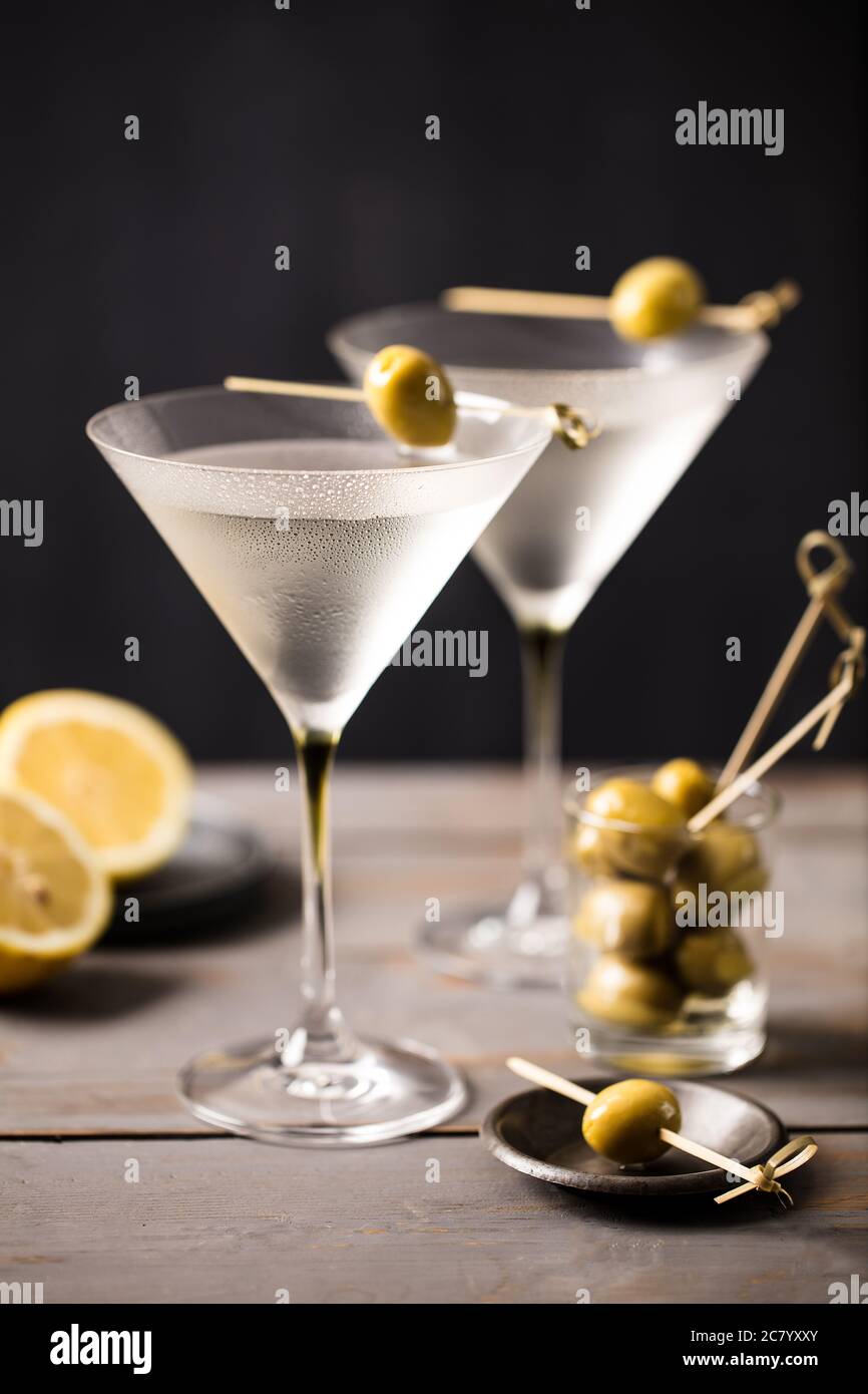 Cocktail martini freddi serviti con un set di olive su un bar grigio in legno con sfondo scuro Foto Stock