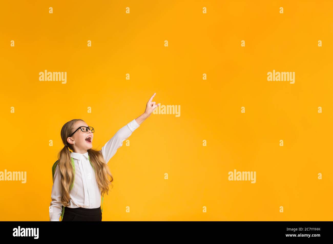 Scuola elementare ragazza che punta dito che posa sopra sfondo giallo Studio Foto Stock