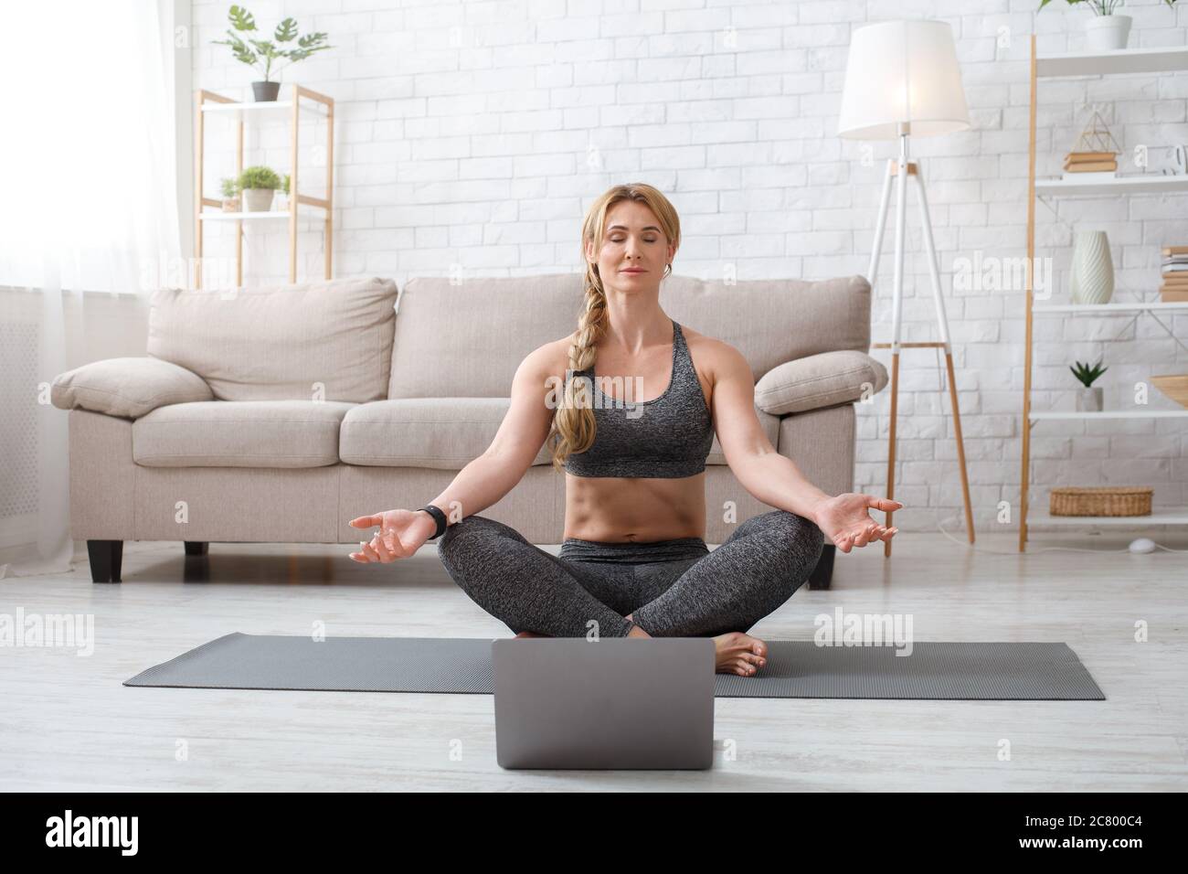 Allenatore online che pratica yoga. Donna in loto posa con occhi chiusi, meditazione sul tappetino sul pavimento Foto Stock