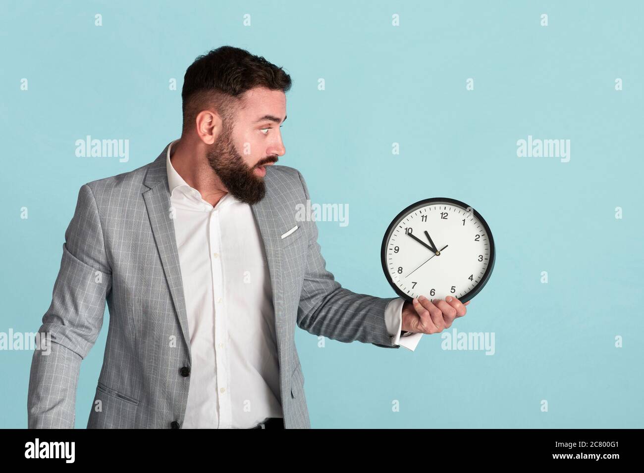 Problema di gestione del tempo. Temuto lavoratore aziendale con orologio analogico mancante scadenza su sfondo blu Foto Stock