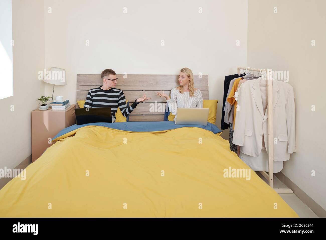 Coppia riposante in letto con computer portatili e chiedendo a vicenda di portare alcuni spuntini e bevande in camera da letto Foto Stock