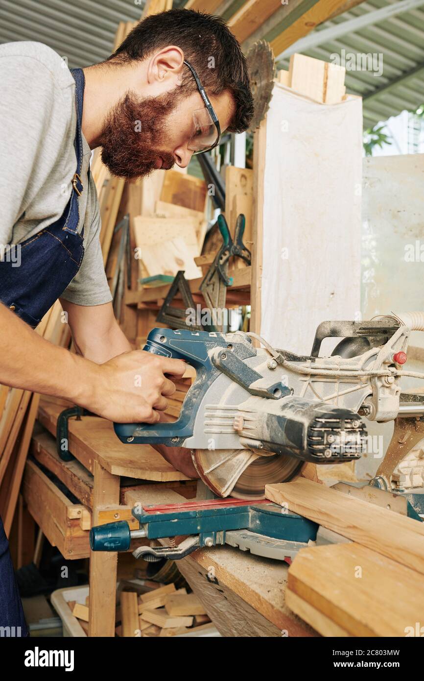 Carpentiere professionale serio che usa sega circolare di azionamento del verme per tagliare le tavole di legno per il suo progetto Foto Stock