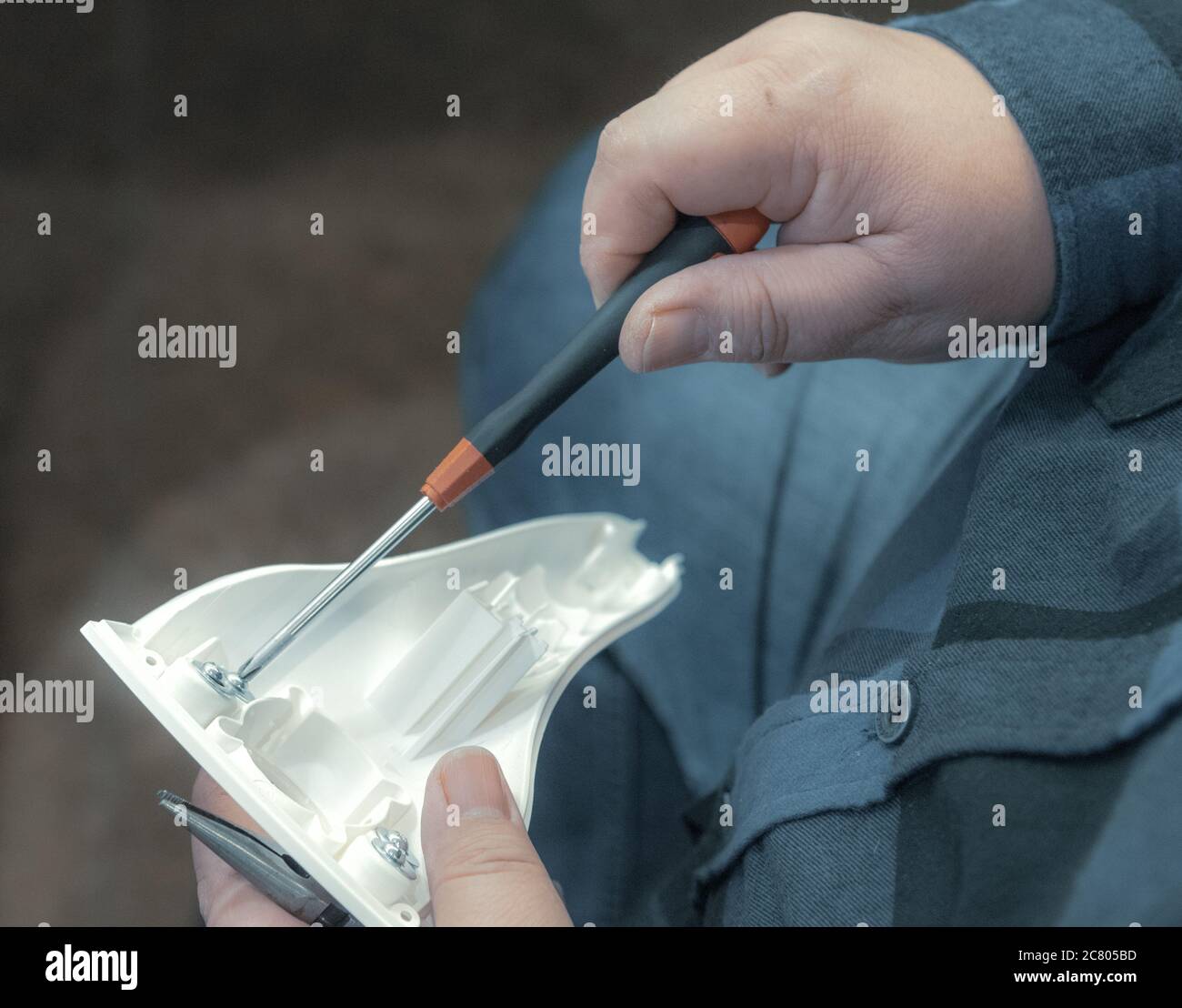 Mani di un tecnico che tiene un cacciavite mentre fissa un dispositivo elettronico Foto Stock