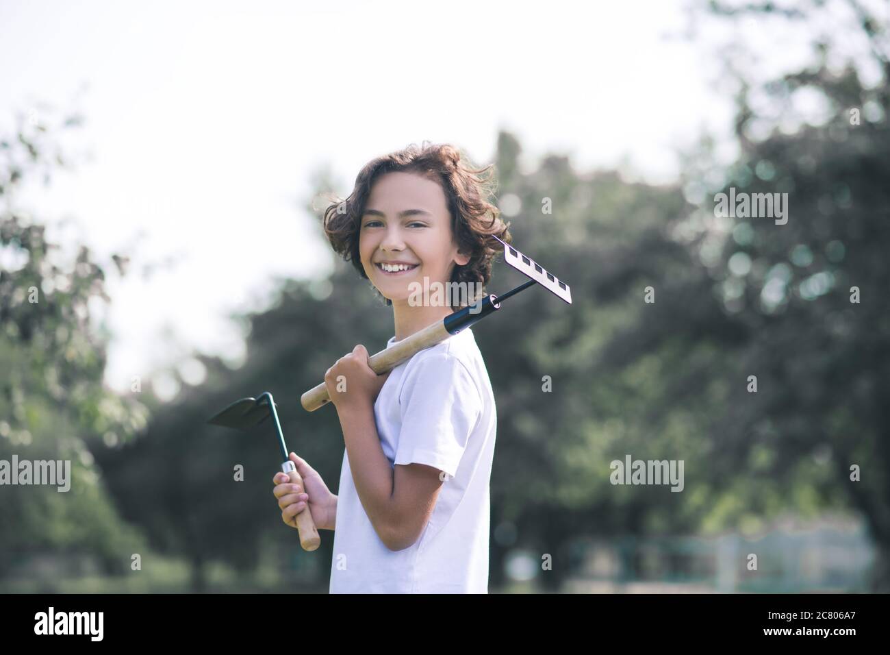 Ragazzo dai capelli scuri che tiene un rastrello e sorride Foto Stock