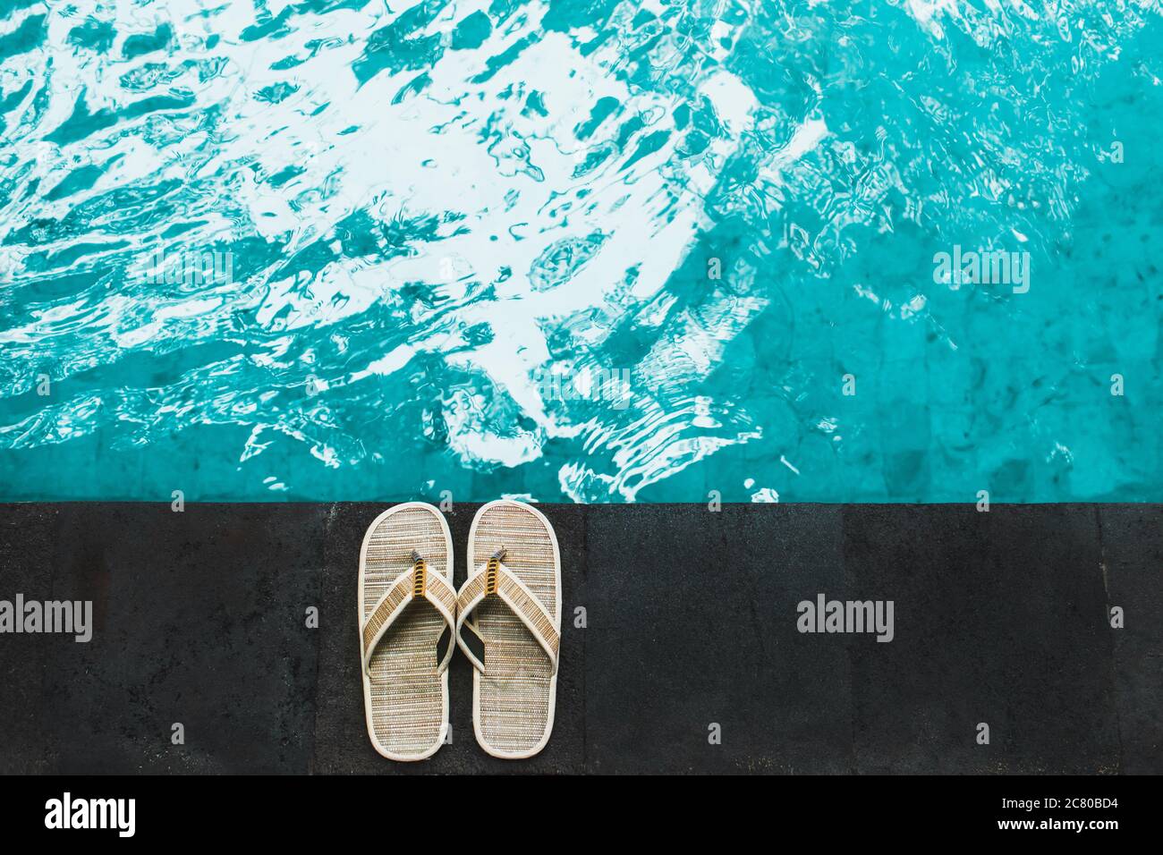 Flip flop in vimini di paglia sulla piscina. Realizzato in materiale naturale, responsabilità sostenibile, monouso. Vacanze tropicali. Foto Stock