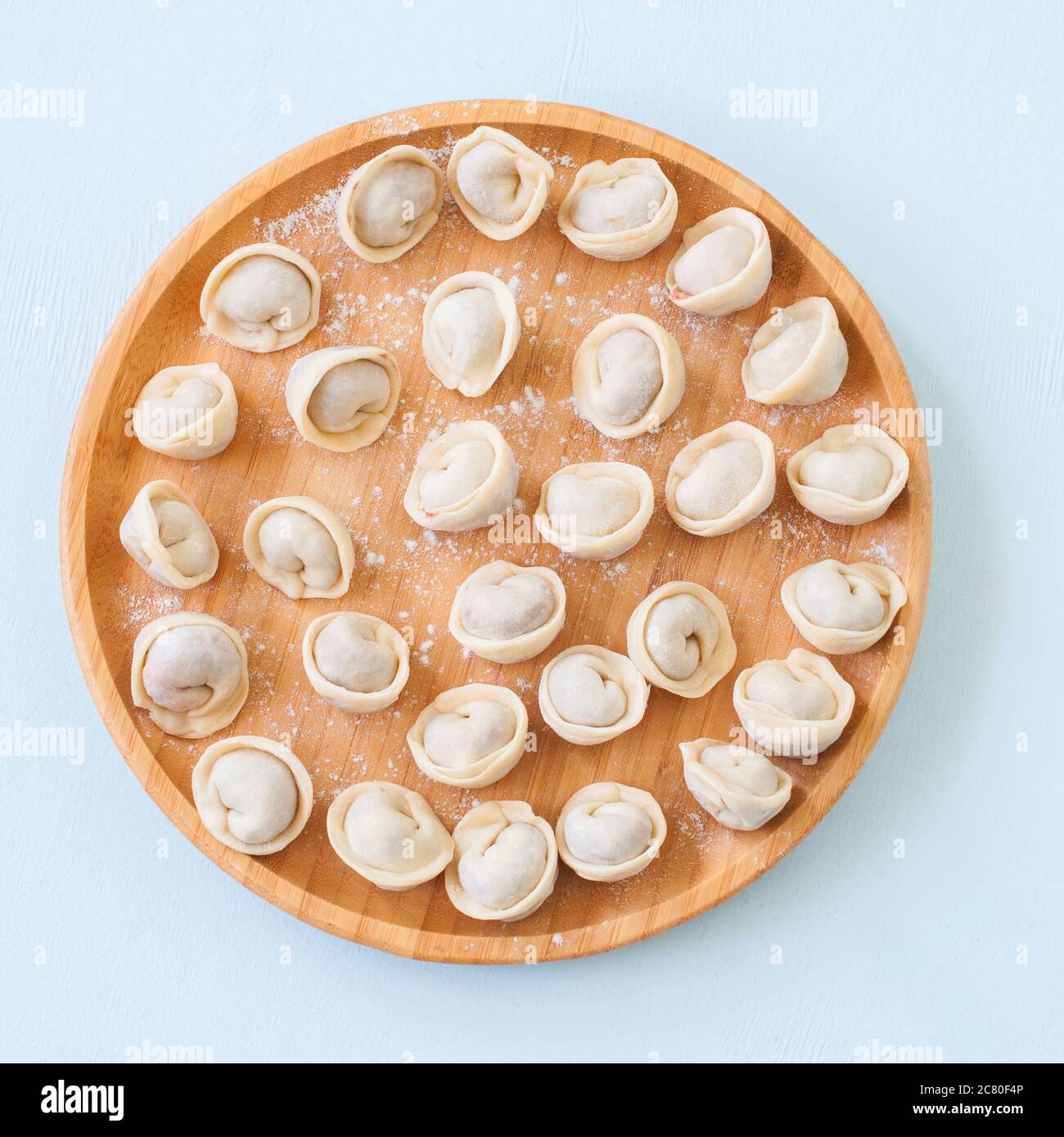 Pelmeni grezzi o gnocchi russi su una piastra di legno. Foto Stock