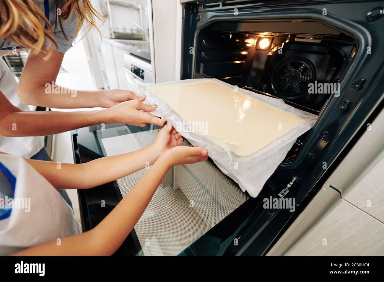 Immagine ravvicinata di madre e figlia che mettono la lamiera da forno calda quando si fa la pan di Spagna a casa Foto Stock