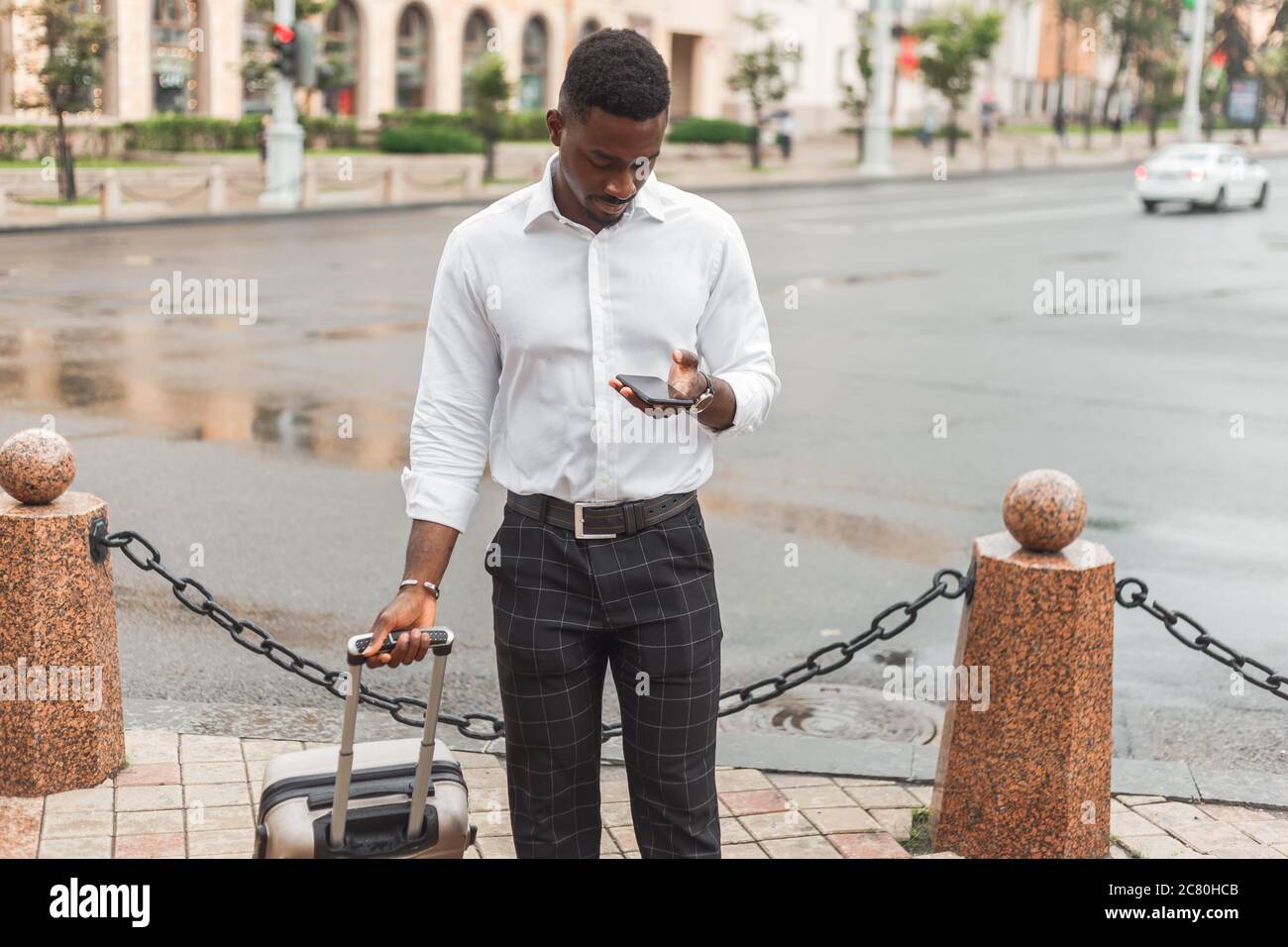 Afro uomo d'affari con bagagli utilizzare il telefono per noleggiare un taxi. Uomo nero in viaggio d'affari Foto Stock